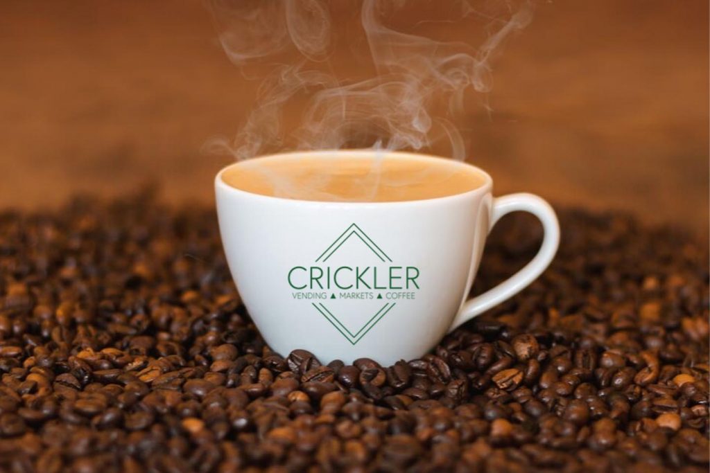 a white coffee cup with the green Crickler logo on top of coffee beans