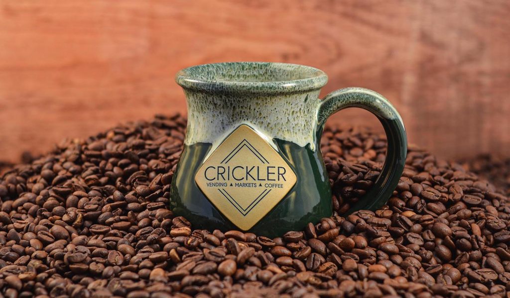 a green mug with the Crickler logo on top of coffee beans