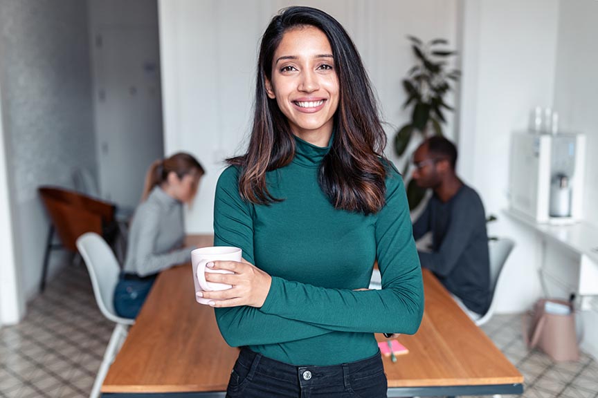 an indian woman standing in an office with a cup of coffee