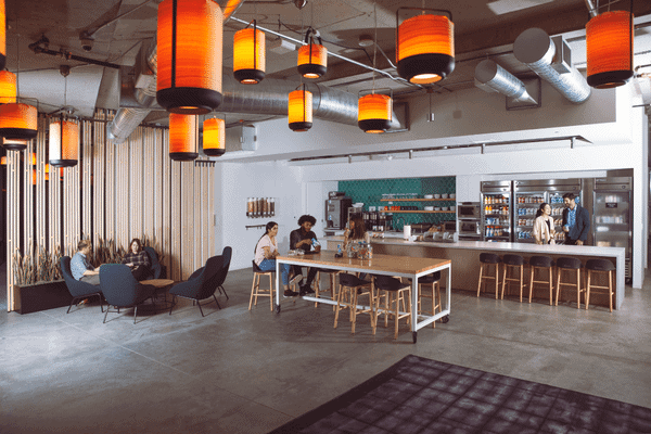 a white shot of an office breakroom area with seating, coolers, coffee, and employees sitting around eating